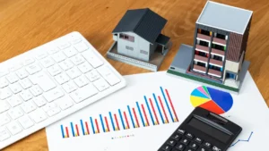 Maquettes d'immeubles avec calculatrice et graphiques financiers pour illustrer la gestion locative et le versement des loyers au propriétaire