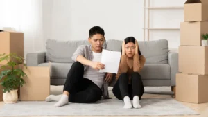 Couple de locataires inquiets lisant un document de mise en demeure pour loyers impayés, entourés de cartons de déménagement