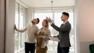 Agent immobilier réalisant un état des lieux d’entrée avec des locataires dans un appartement lumineux, inspection des murs et équipements avant emménagement en 2026.
