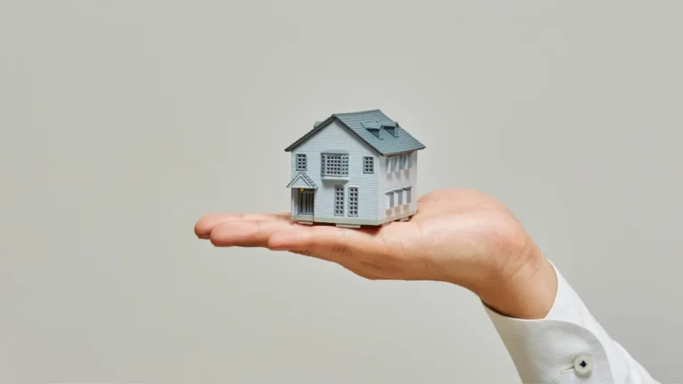 Main tenant une maquette de maison, illustration de l’identifiant fiscal du logement et des démarches administratives immobilières en 2026.